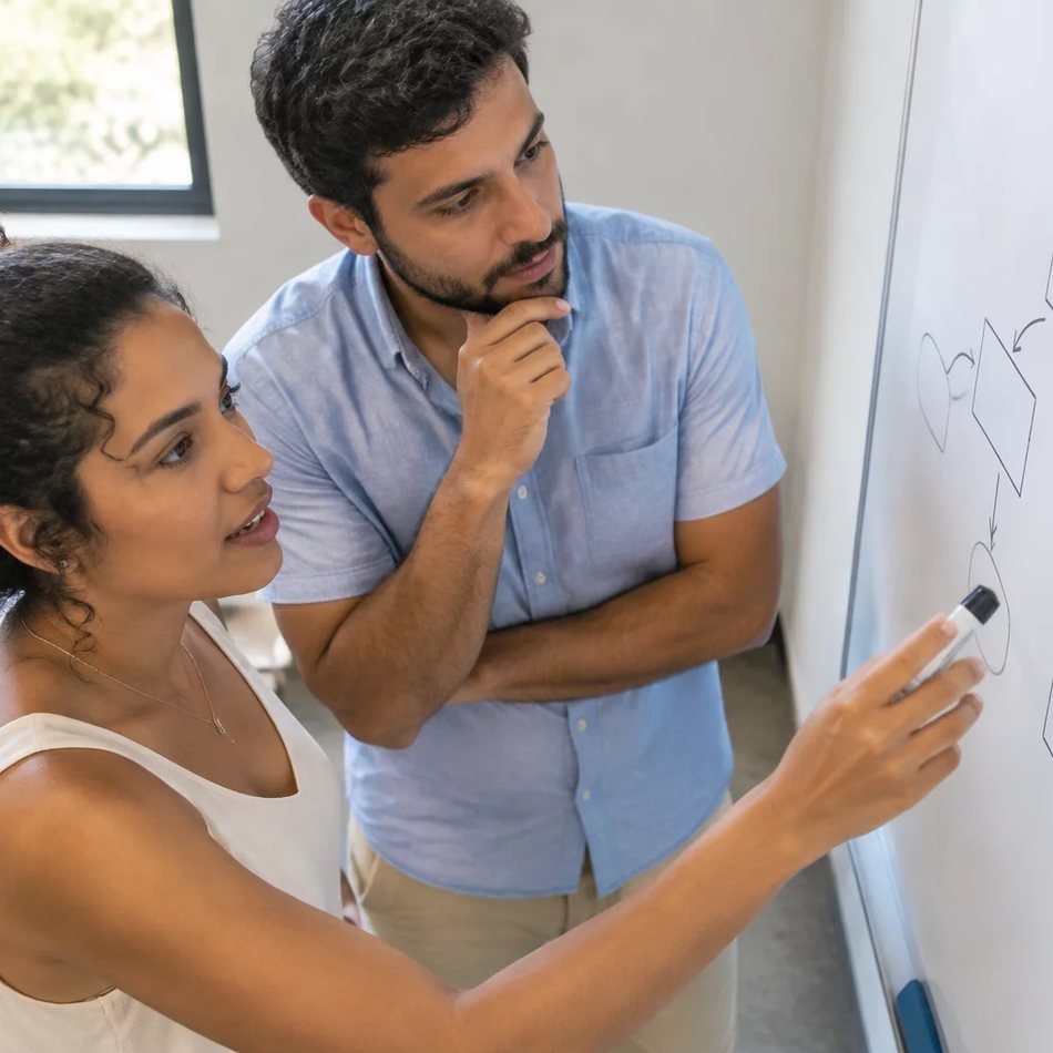 Duas participantes de pé junto ao quadro branco, desenhando as partes de um argumento